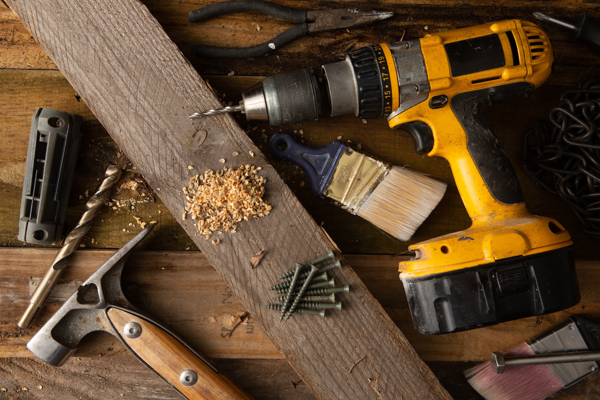 A wooden table is covered in a diverse selection of tools, such as wrenches, saws, and drills.