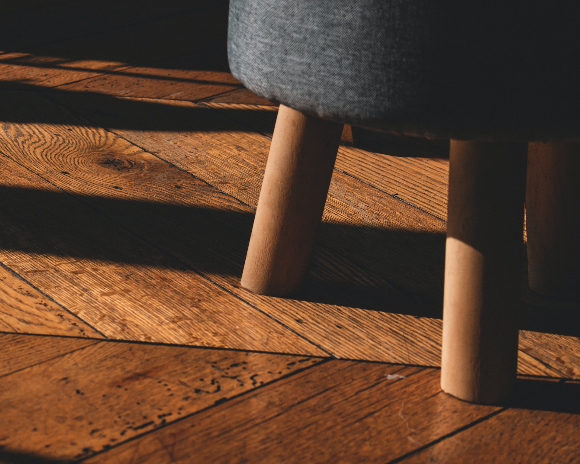 The legs of a stool are seen standing on a beautifully crafted wooden floor.